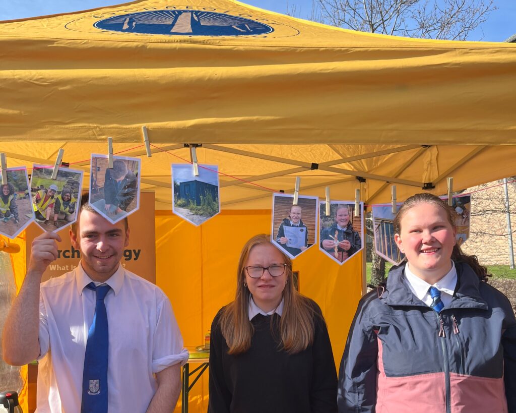 Three smiling people standing under a yellow gazebo with bunting by their heads.