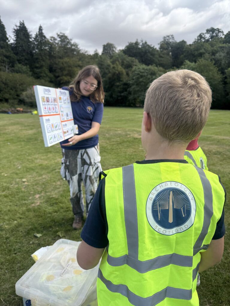 A child in a hi-vis yellow vest is looking at a person in a blue tshirt holding up a board.