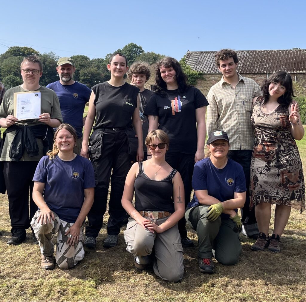 10 smiling people standing in the sun. One of them is holding up a certificate.
