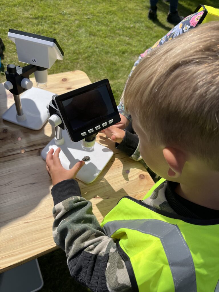 A child in a yellow hi-vis vest is looking at a small piece of coal under a microscope.