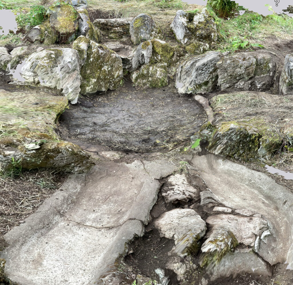 A screenshot of a 3D model of the rockery. There is a central pond filled up with earth, with two concrete gullies curving away to the bottom of the photo. Around the central pond are grey rocks with green moss.