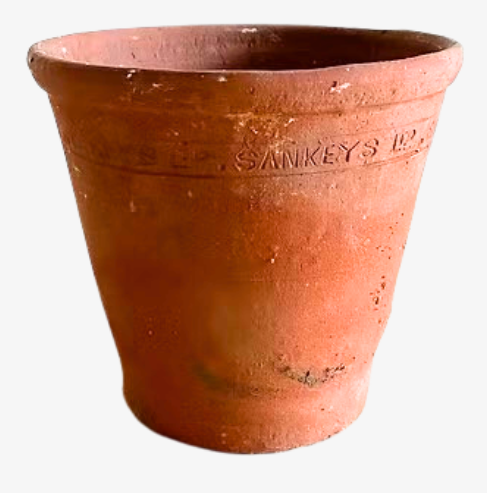 A reddish orange flowerpot is on a plain white background. The pot is reddish orange with some marks and soil. It is empty. On the outside near the top there are letters that have been stamped in, including 'SANKEYS'.