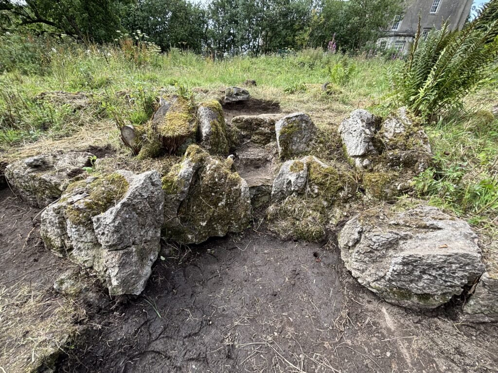 At the bottom is the brown earth. In a curve around the earth are large rough grey rocks with green moss on them. There are stepped stones going up the middle, with plants surrounding the rocks.